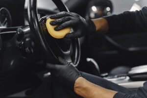 Man in a garage. Worker polish inside a car. Man in a black uniform.