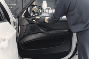 Man in a garage. Worker polish inside a car. Man in a black uniform.